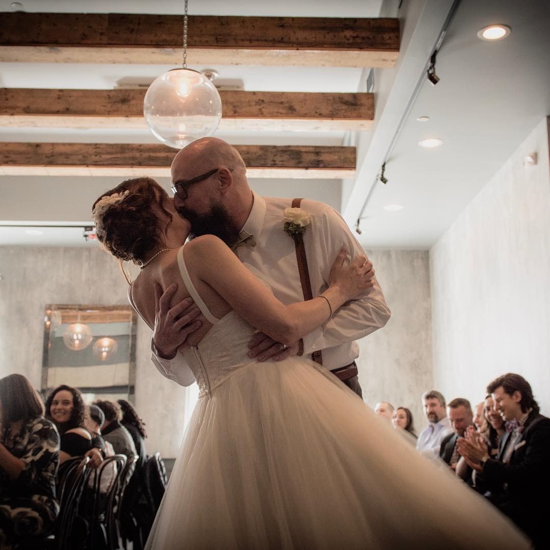 A couple shares their first dance at a wedding reception under exposed wooden beams.