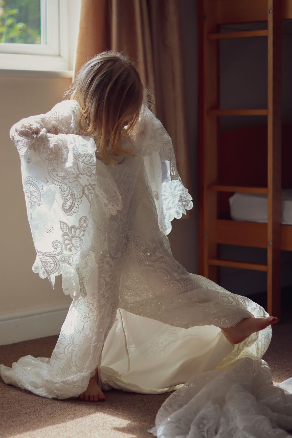 Someone trying on an intricate lace wedding dress in soft natural window light.