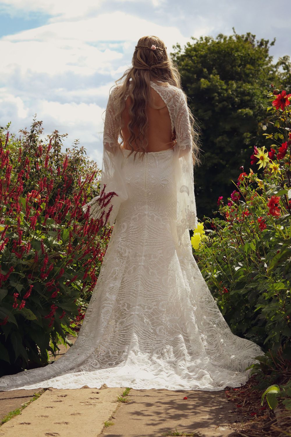 Back view of lace wedding dress with long train amid colorful garden flowers.