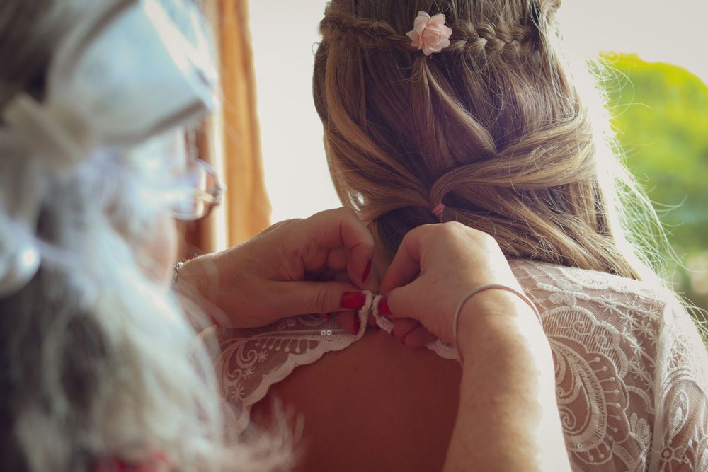 Close-up of someone helping fasten a wedding dress with delicate details.