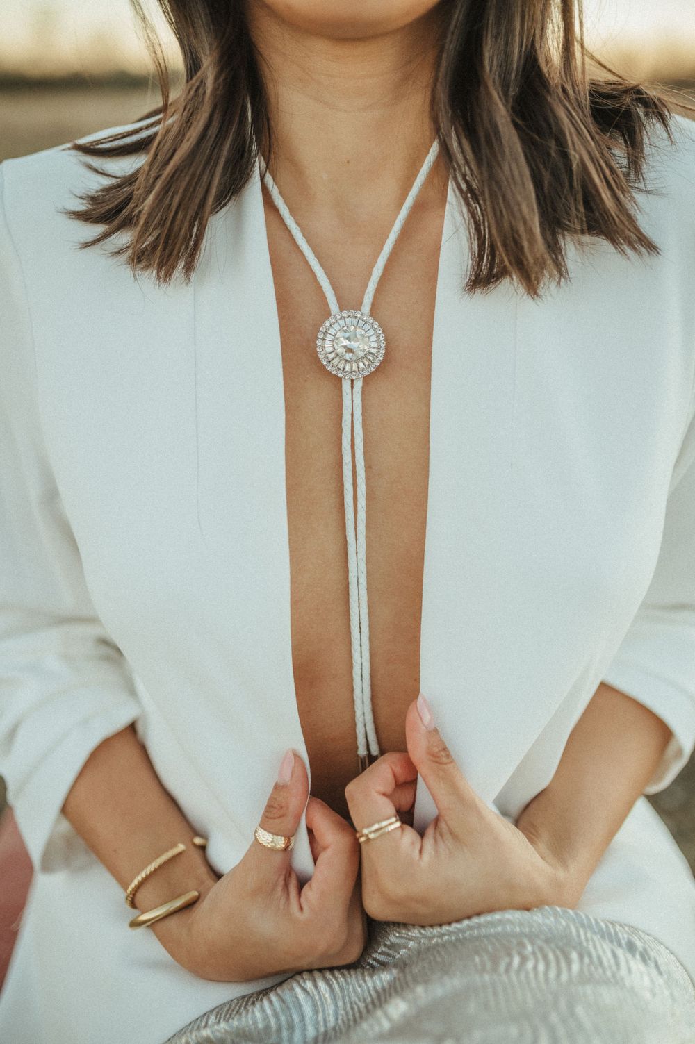 Close-up of silver bolo tie necklace and rings on woman wearing white blazer.