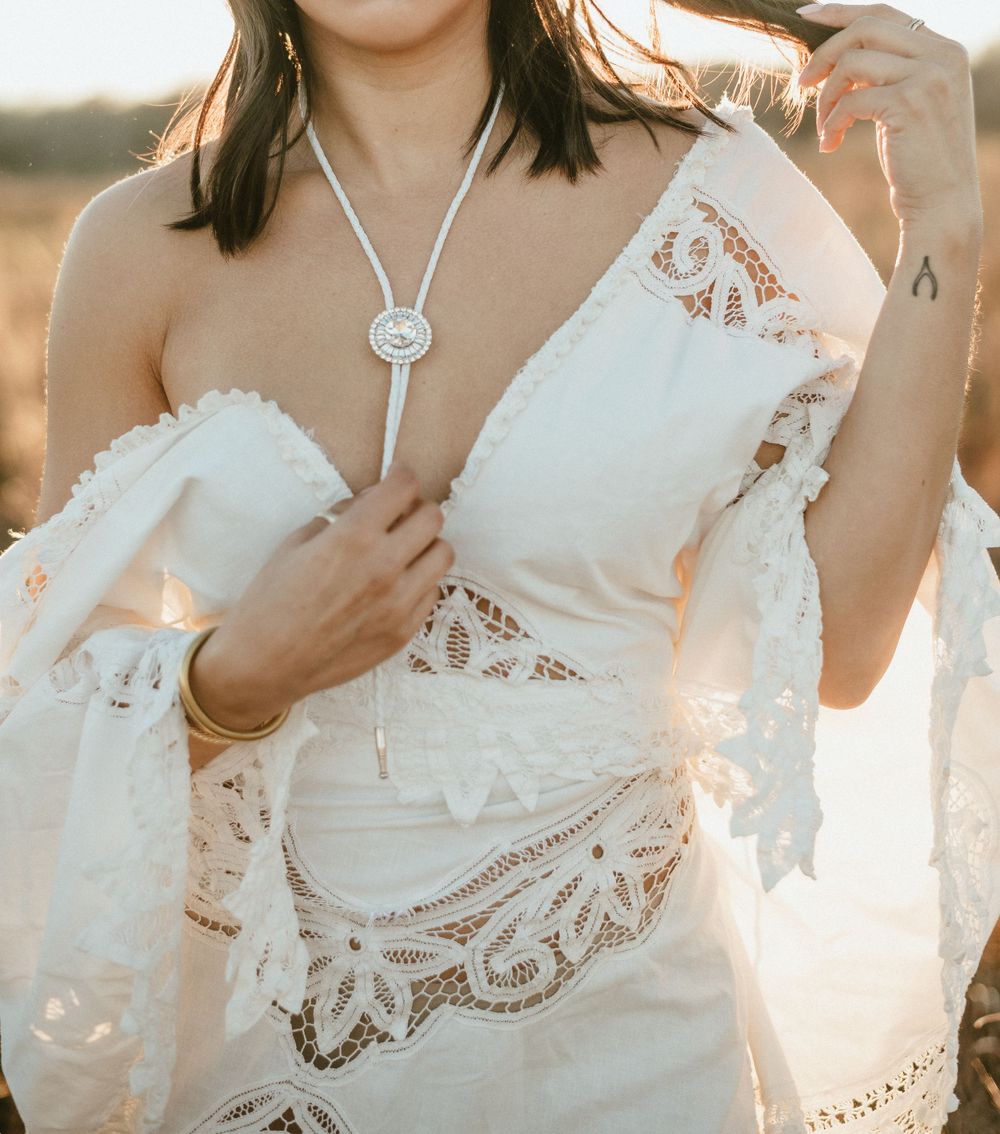 Detailed view of lace wedding dress and silver bolo tie necklace in warm sunset light.