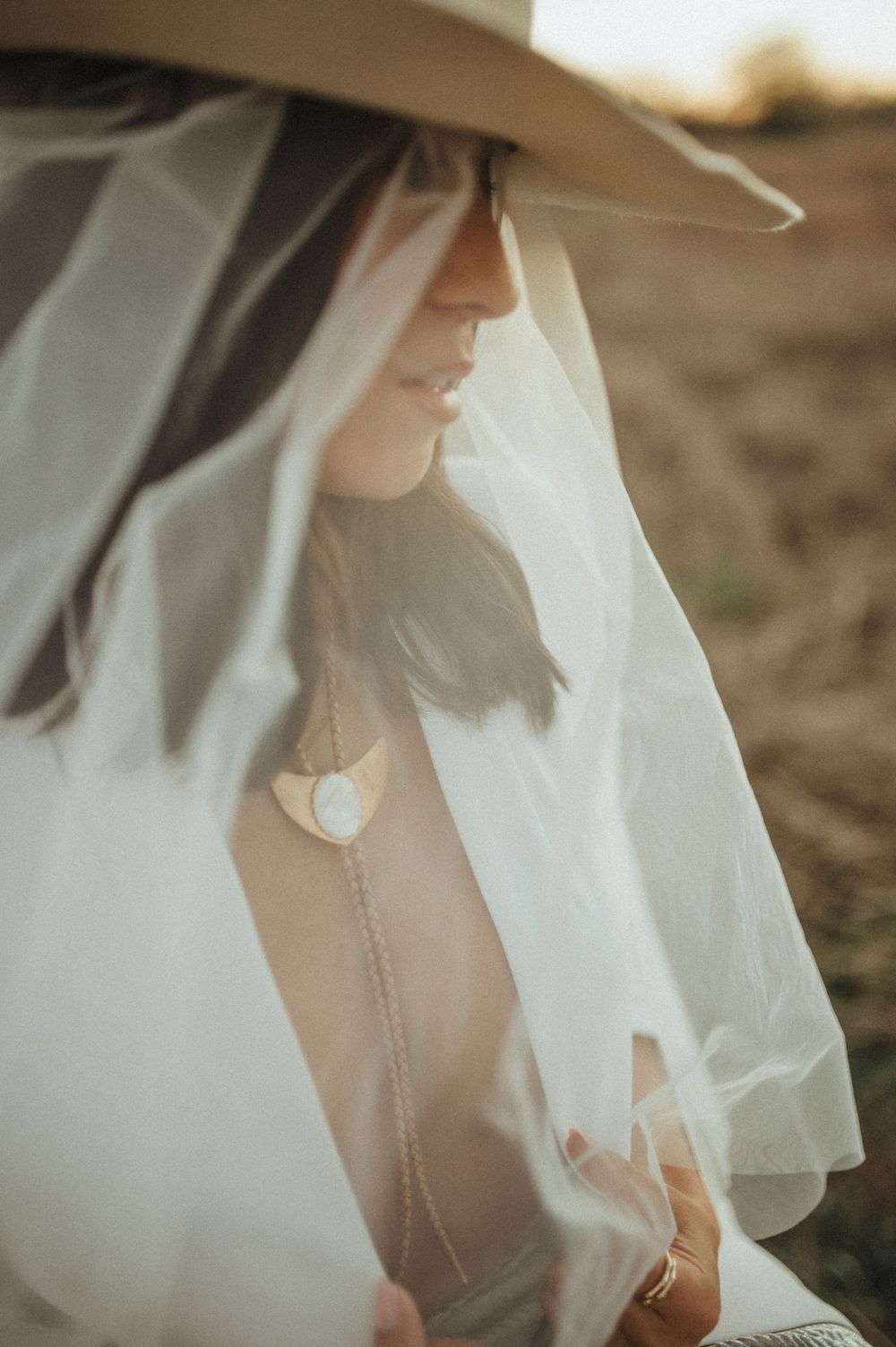 Romantic side profile with flowing veil and western hat at sunset.
