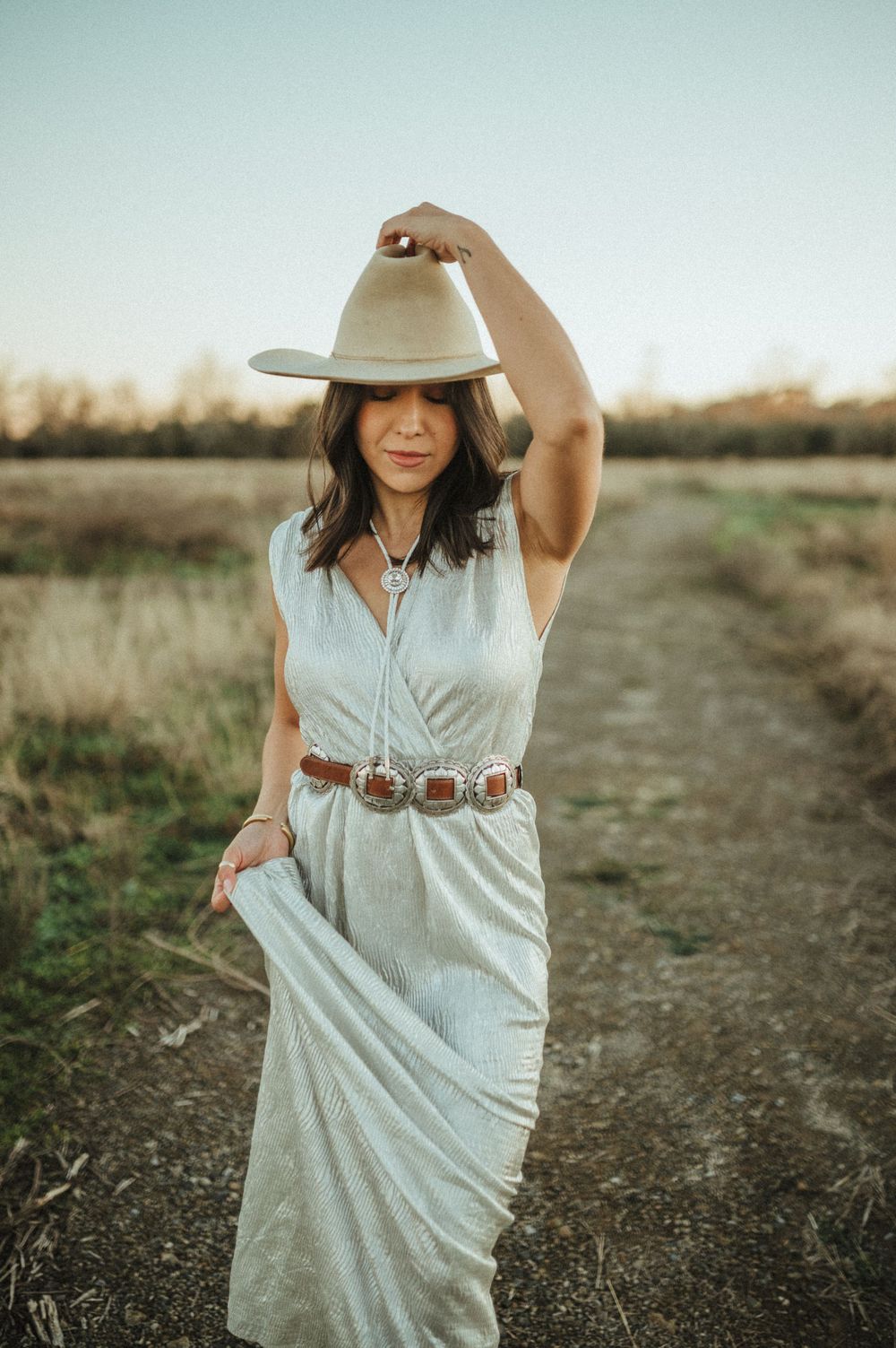 Western-styled fashion shot featuring white dress and concho belt on dirt path.