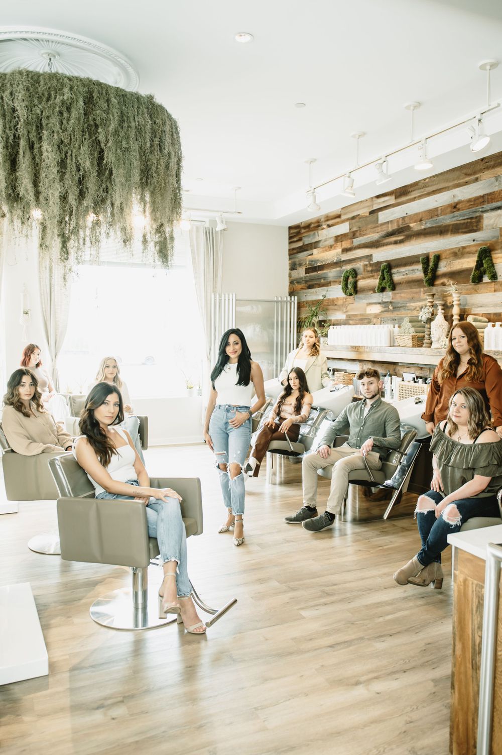Modern salon interior with hanging plants and wood accent wall where people gather in casual attire.