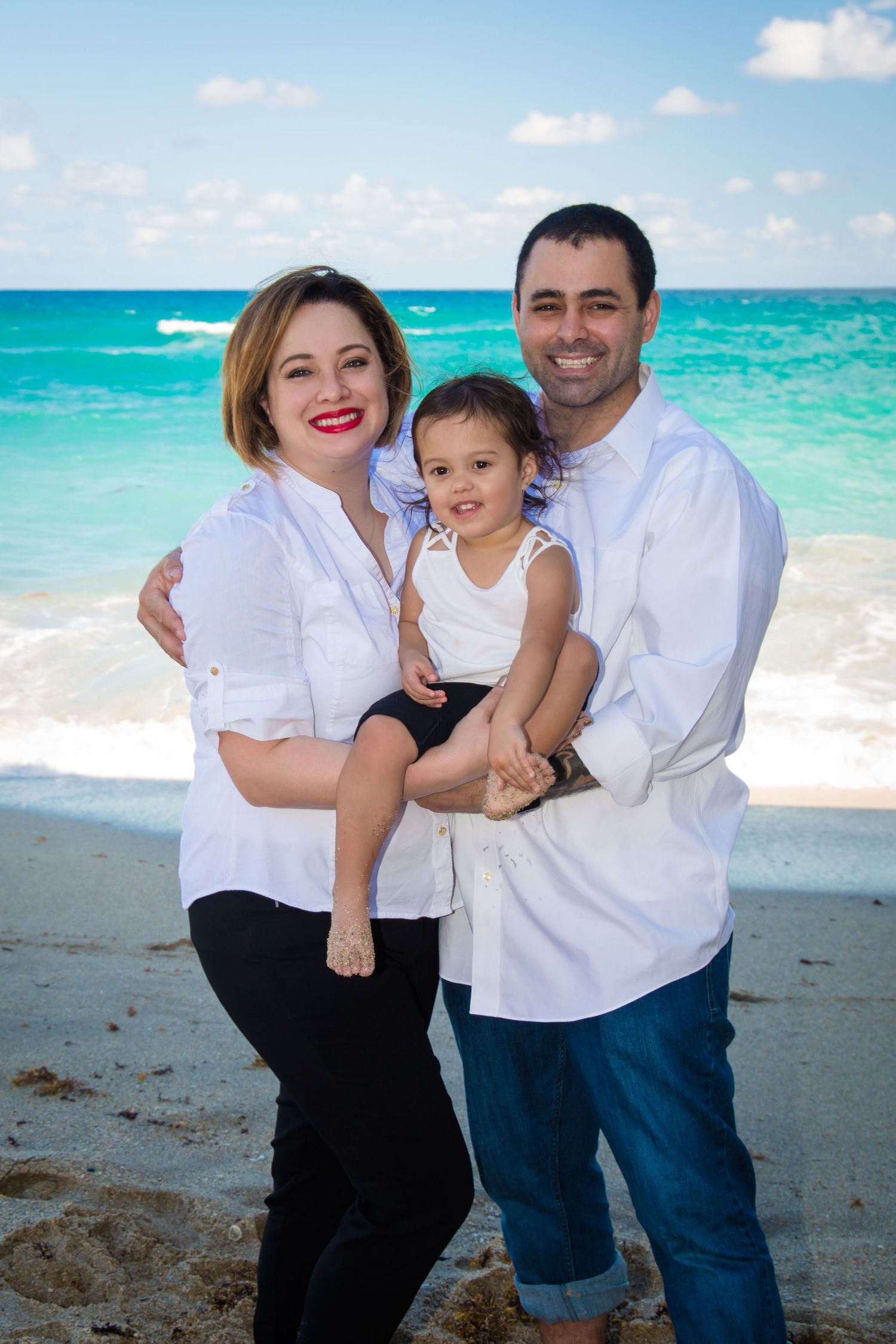 Family enjoying a sunny day at the beach with turquoise waters and white sand in the background.