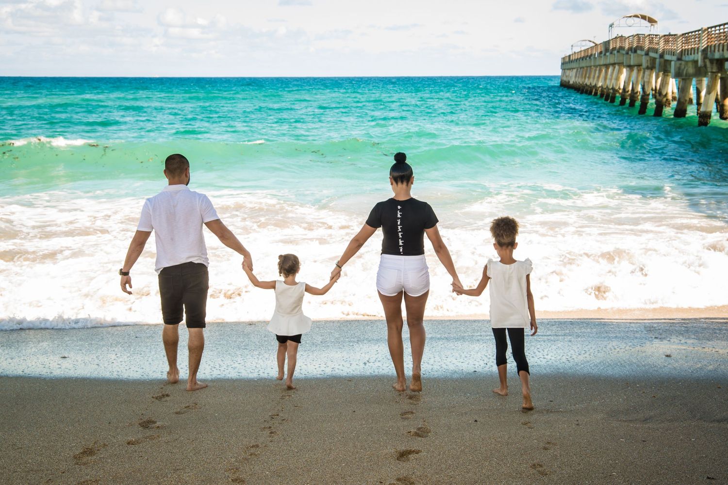 Group silhouettes walking along a tropical beach with pier and crystal blue waters.