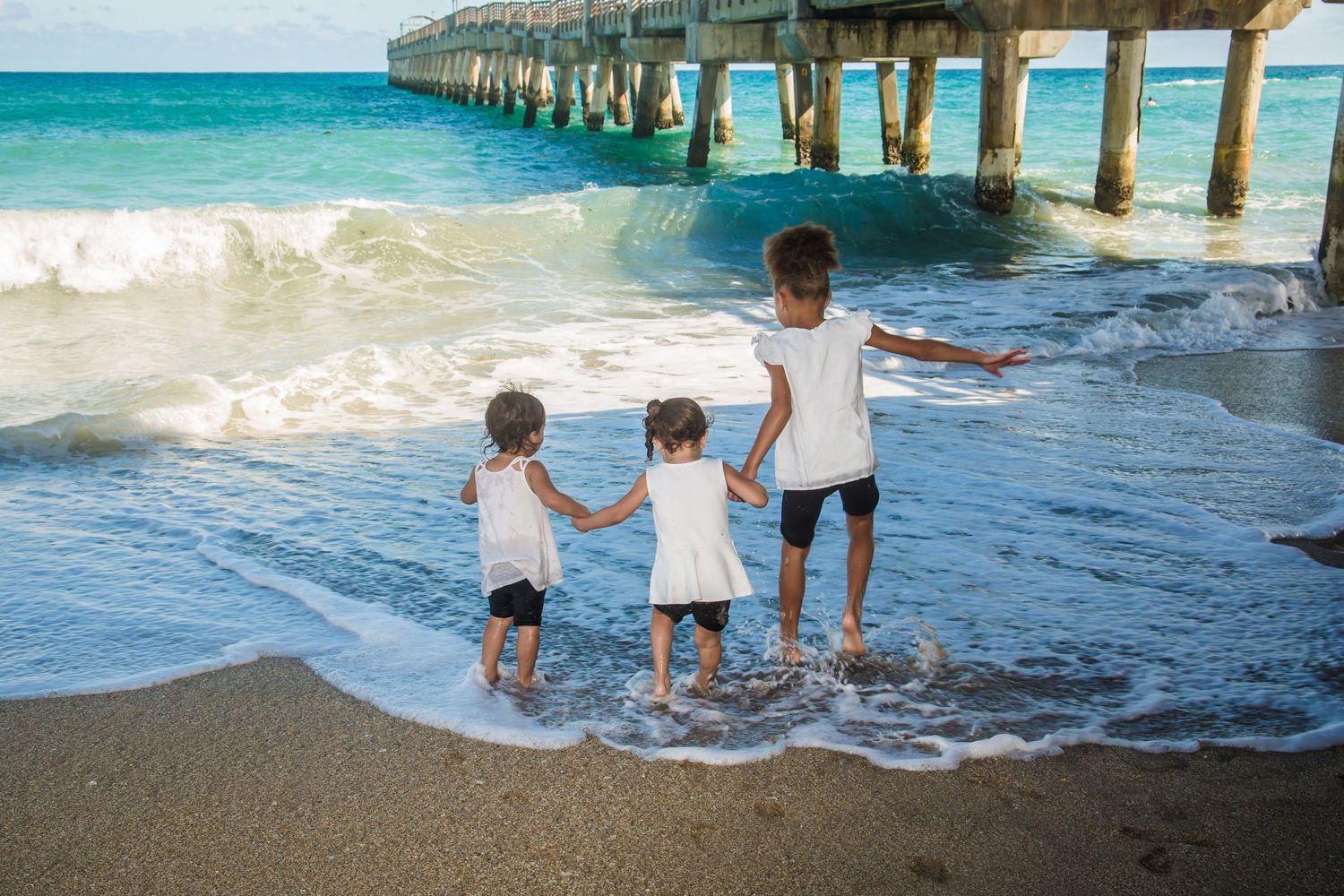 Children playing at the edge of ocean waves near a wooden pier.