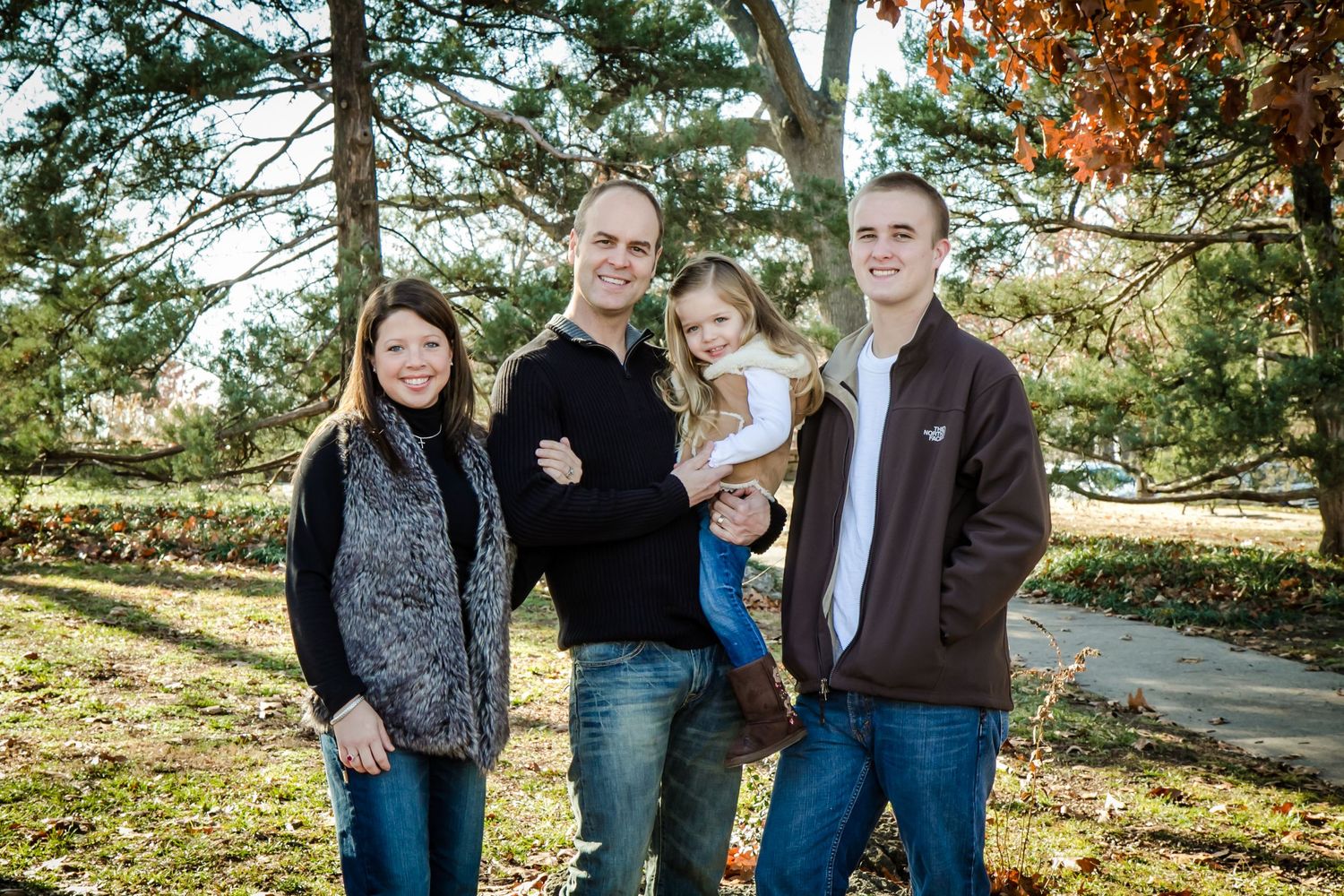 Family of four posing together in a sunny autumn park setting.