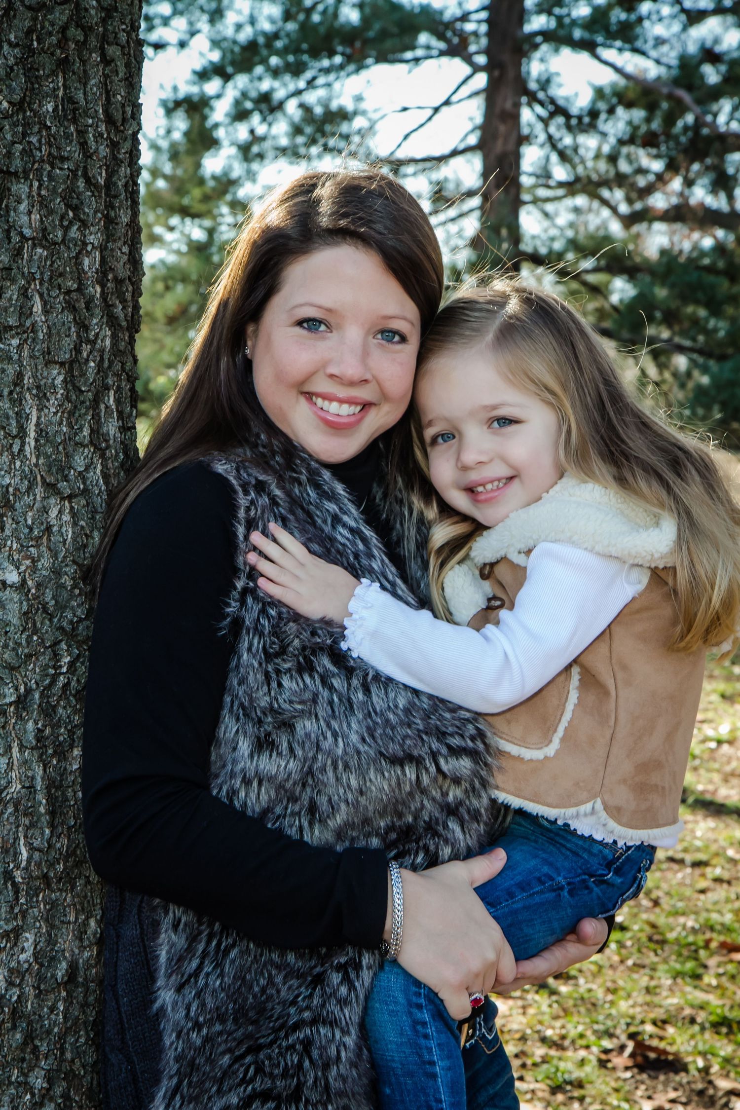Mother and daughter embracing by a tree in a sunny outdoor setting.