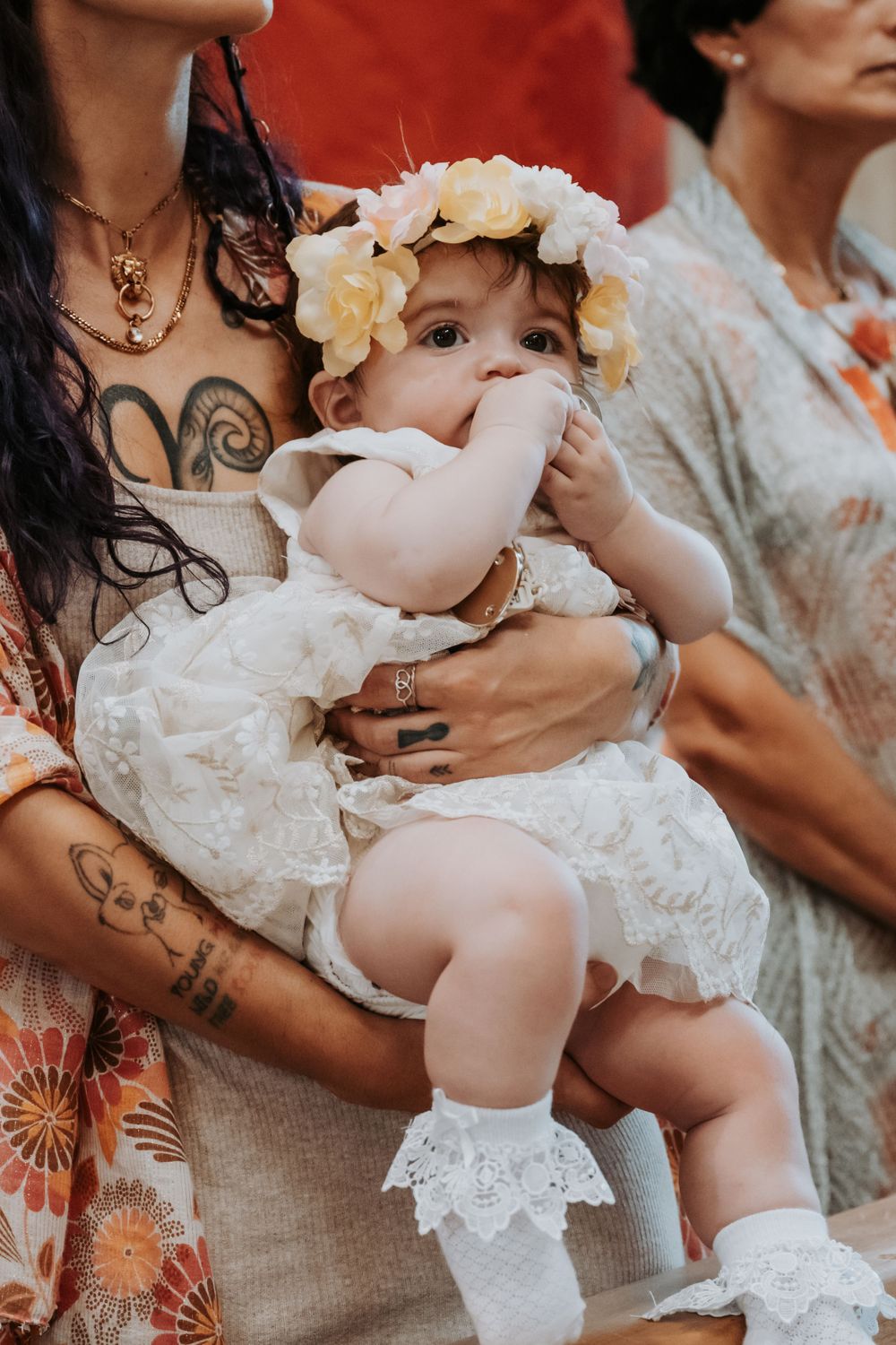 Sweet moments of a baby in white lace baptismal dress being held in floral-patterned arms.