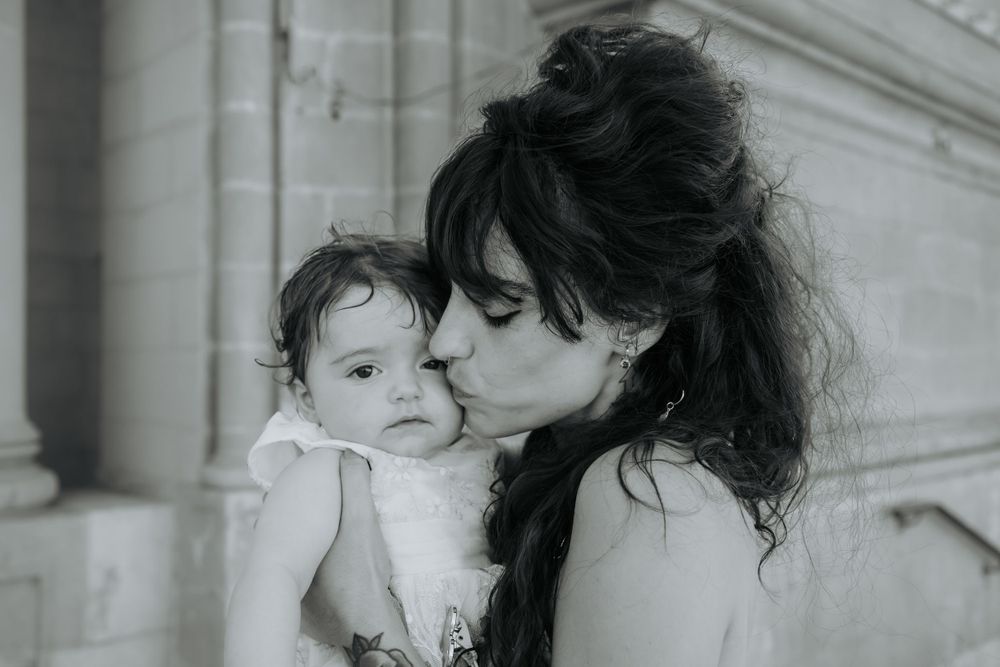 A tender black and white portrait showing an intimate parent-child moment against a light background.
