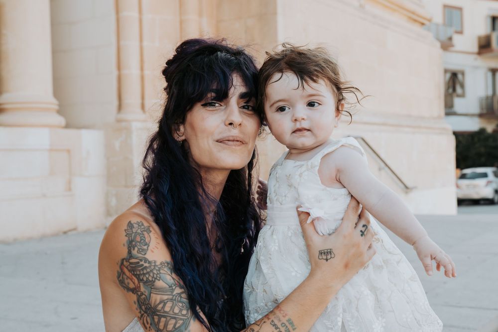 Mother and child in white outfits sitting by classic architectural columns.