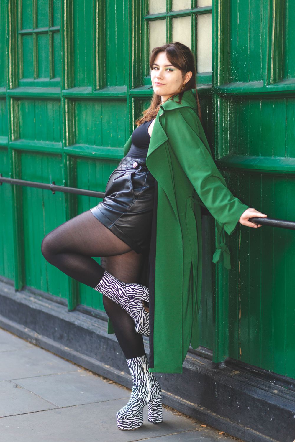 Model Beata dressed in a green raincoat posing against a London taxi rank of the same green colour