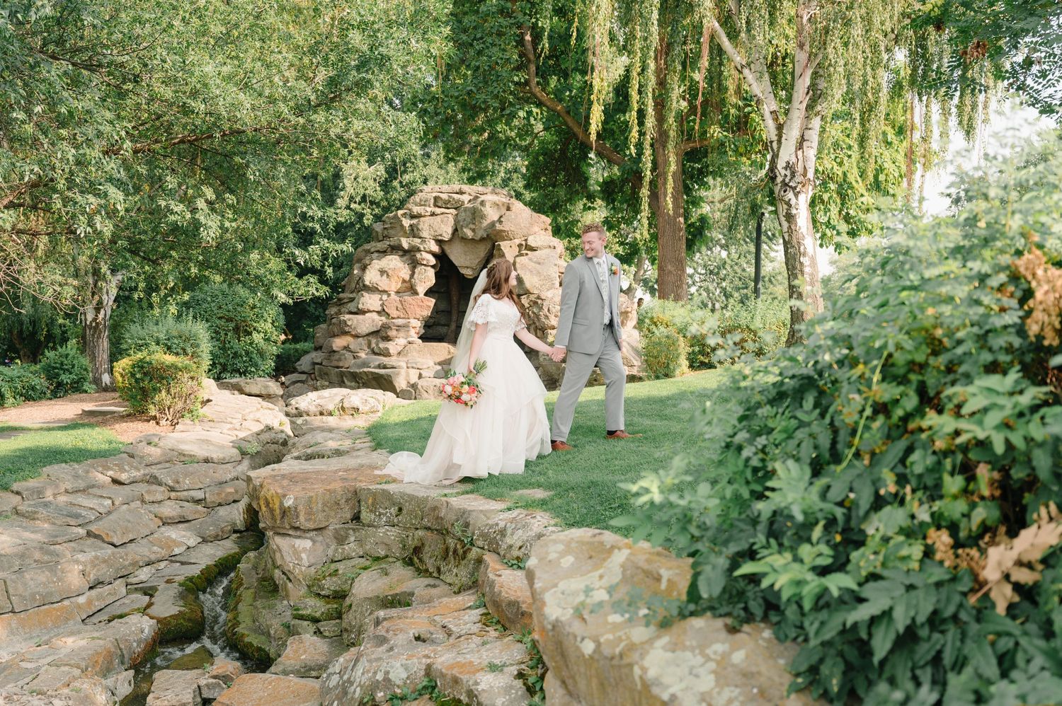 Couple walking through stone archway in lush garden setting.