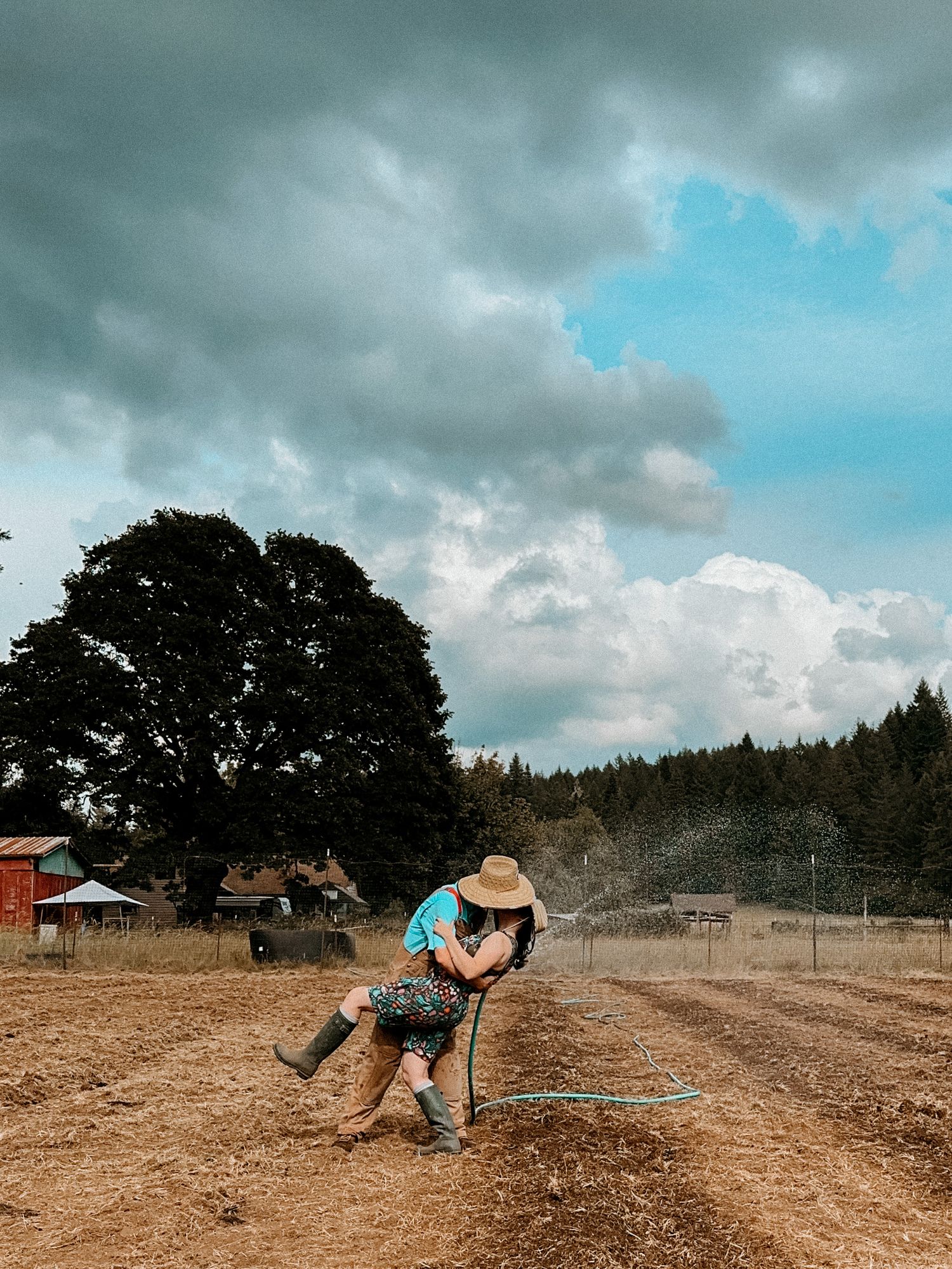 Two people practicing acrobatic moves in a dusty field under dramatic clouds.