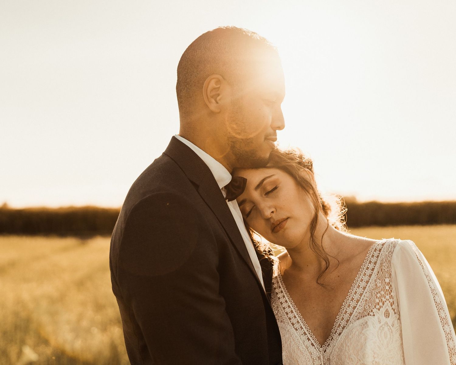 A romantic sunset moment between a couple in formal wedding attire in a golden field.