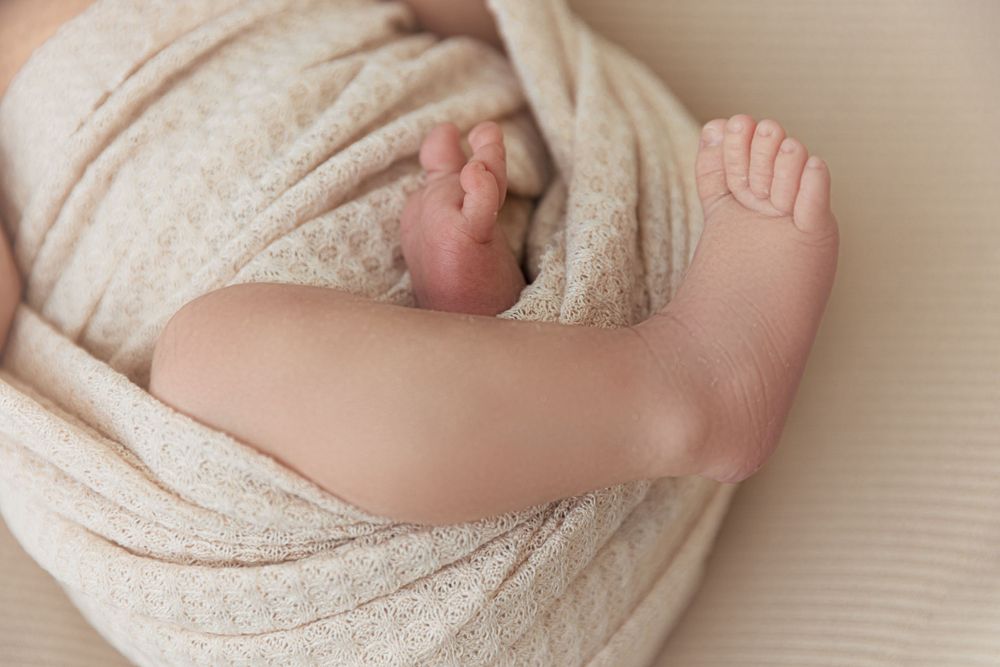 Close-up of tiny baby feet wrapped in soft beige blanket.