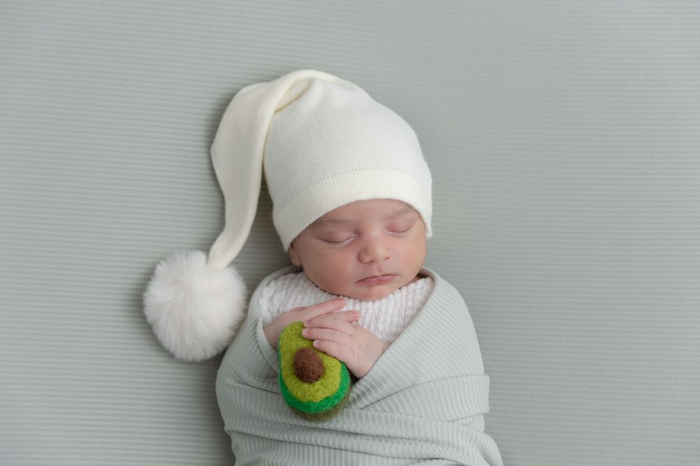 Peaceful sleeping baby wrapped in grey swaddle wearing white winter hat with pom pom.