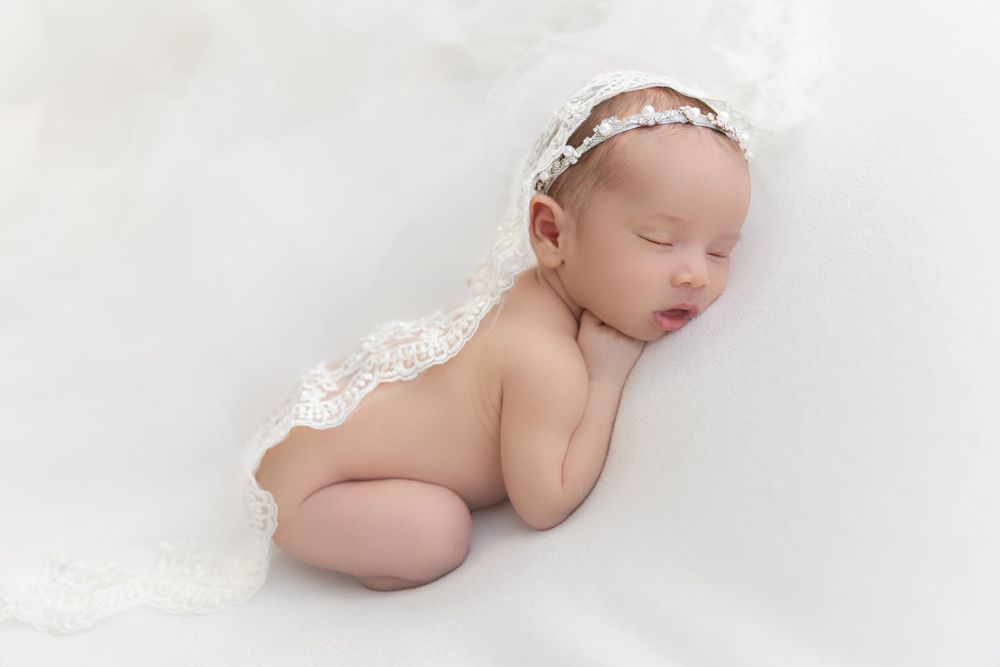 Sleeping newborn baby wearing delicate lace headband on soft white blanket.