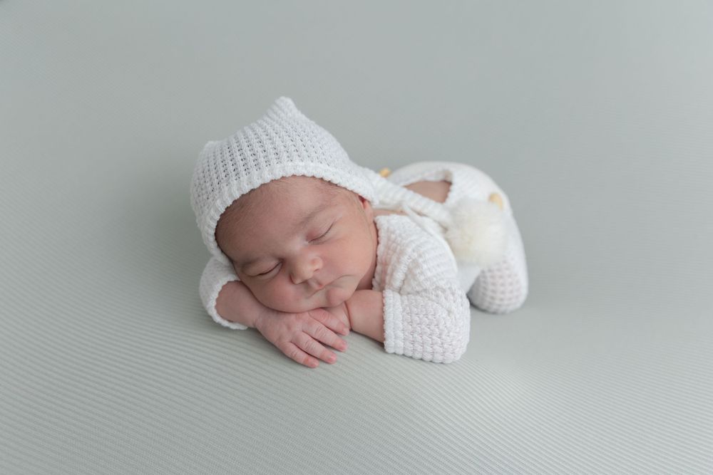 Sleeping newborn in cozy white knit outfit on grey backdrop.