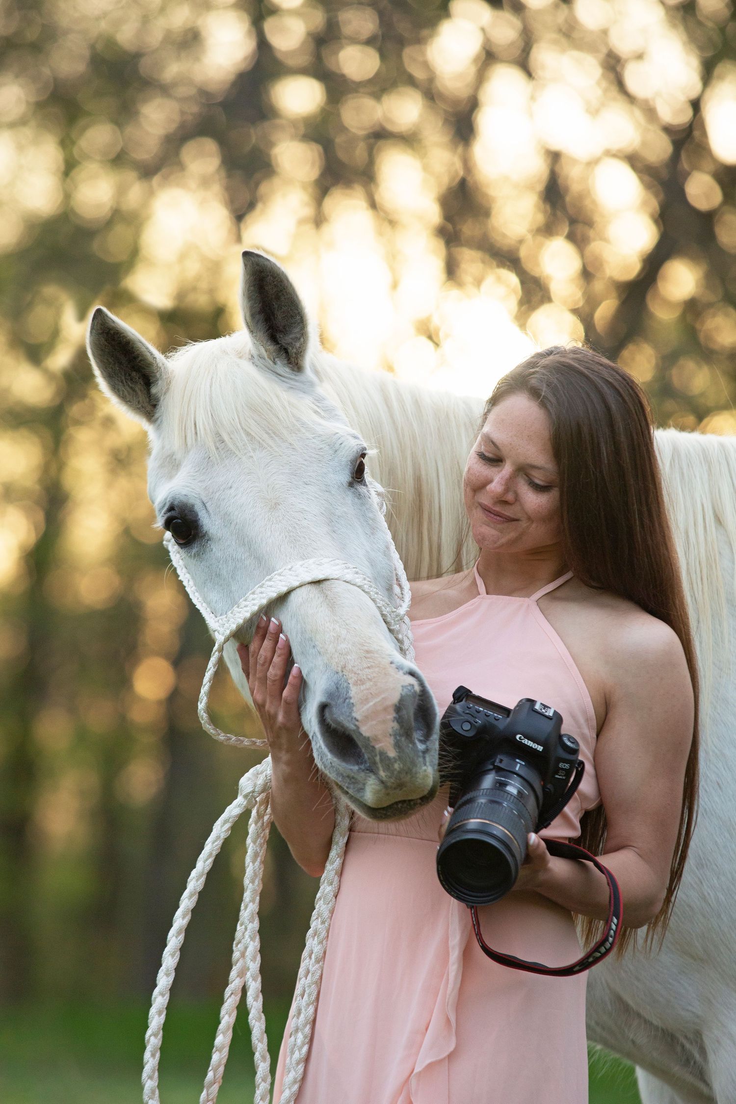 girl holding a camera standing next to a white horse