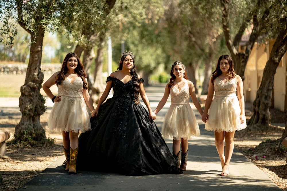 Formal group photo with black ball gown and white dresses in a tree-lined path.