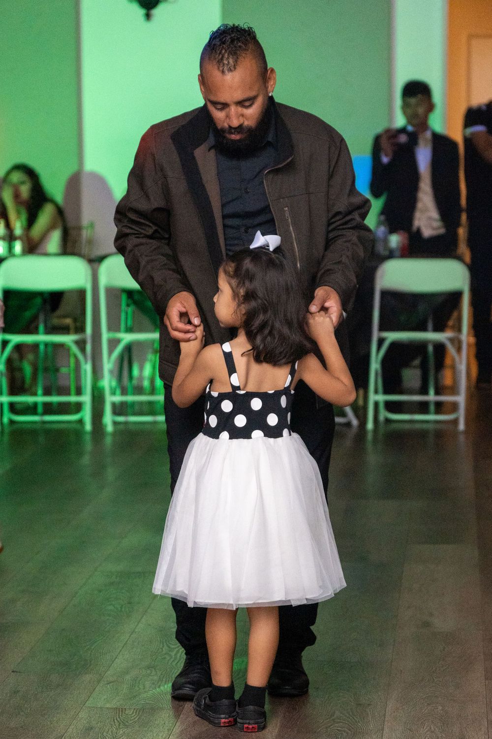 A sweet father-daughter dance moment on a green-lit dance floor, with the little girl wearing a polka dot dress.