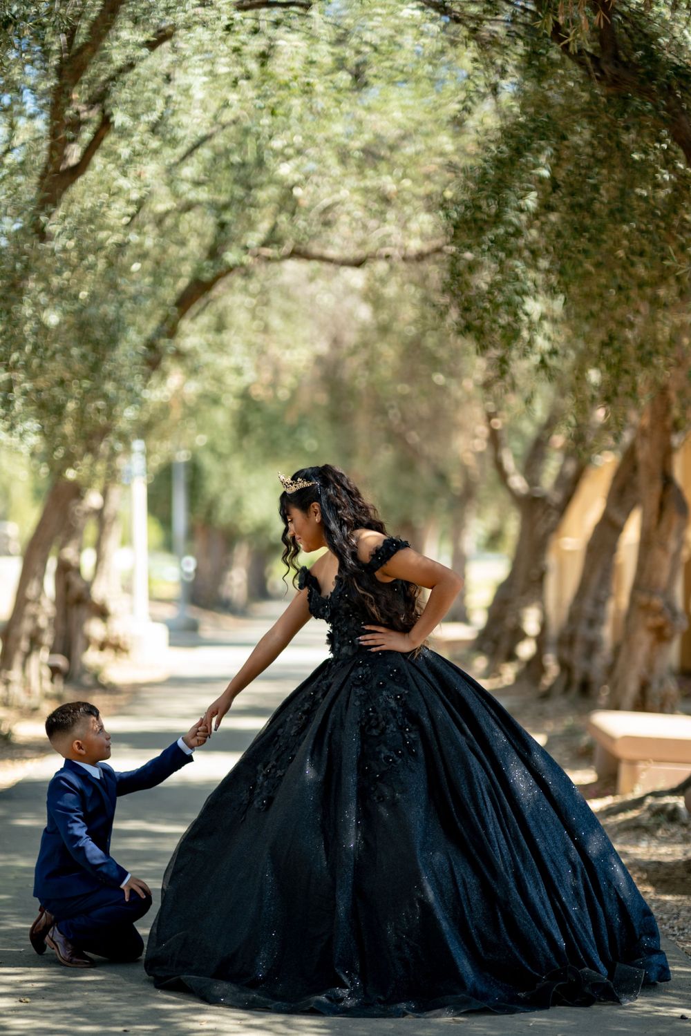 Sweet moment captured on a tree-lined path with formal attire and elegant black gown.
