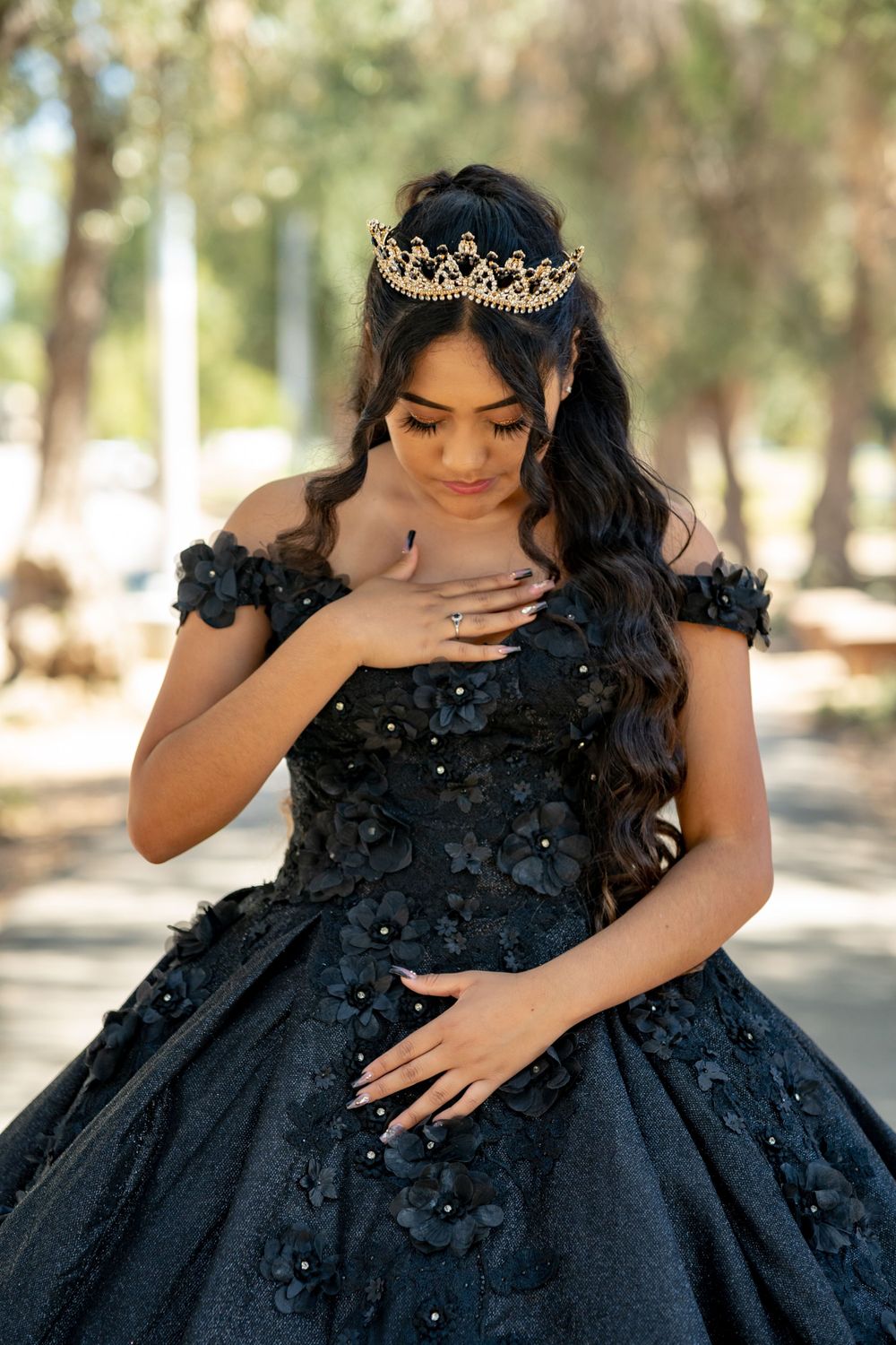 Elegant black ball gown with intricate beading and a golden crown tiara in an outdoor setting.