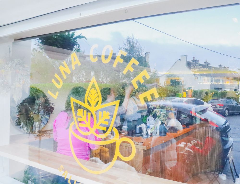 A coffee shop window with bright neon signage reflecting in the glass.