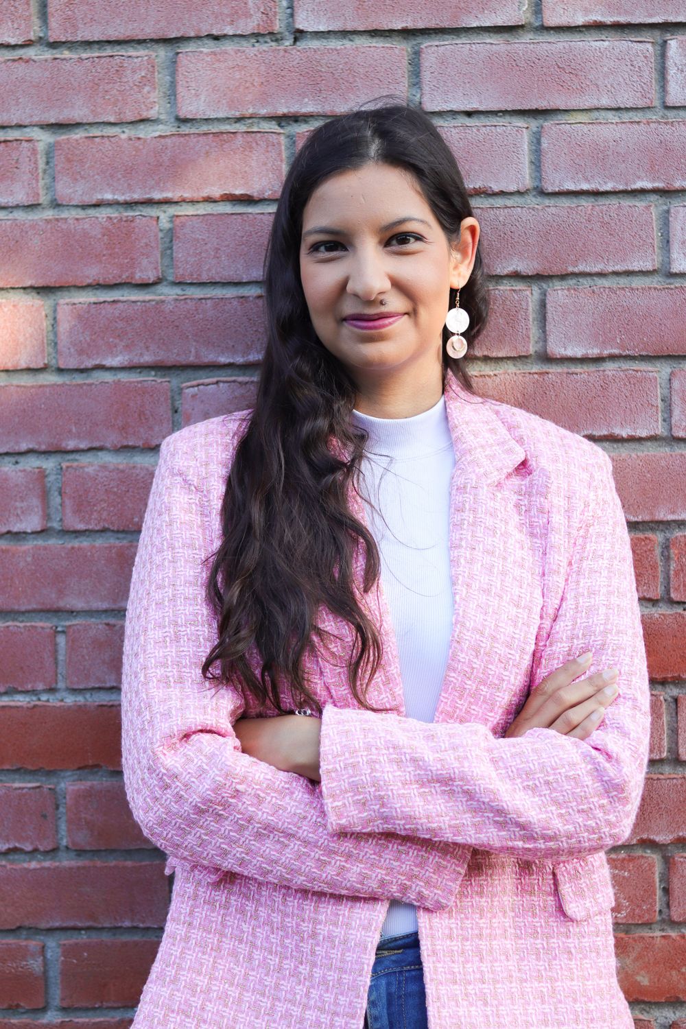 Professional portrait featuring a pink tweed blazer and white top against a brick wall background.