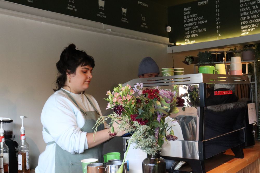 A florist working with fresh flowers at a counter in a coffee shop setting.