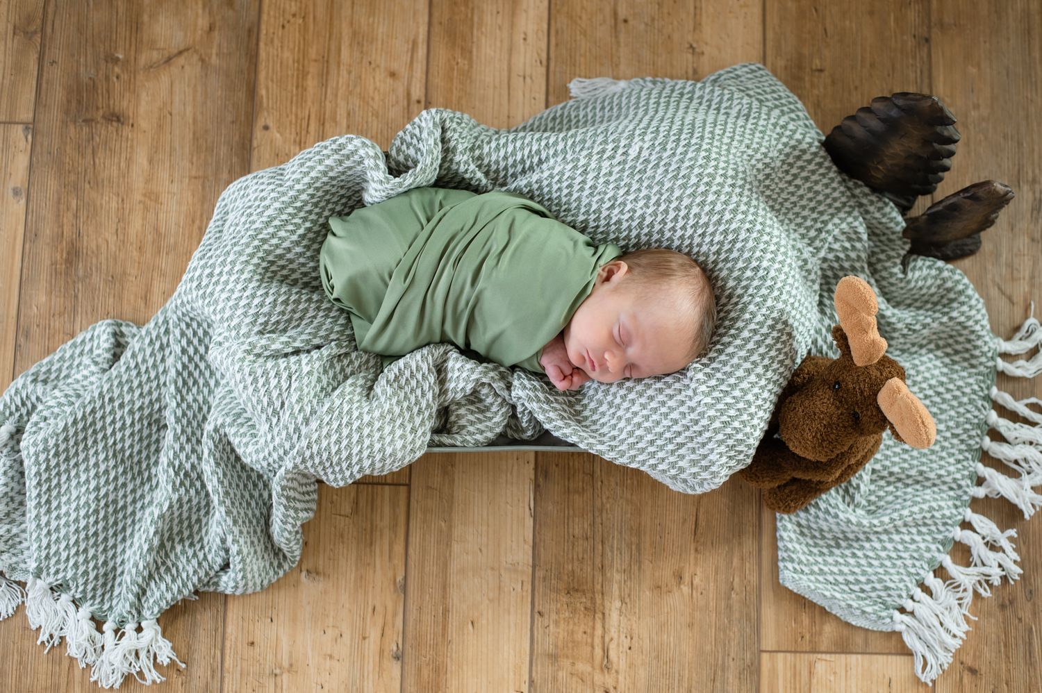 A sleeping baby wrapped in mint green blankets on hardwood flooring.