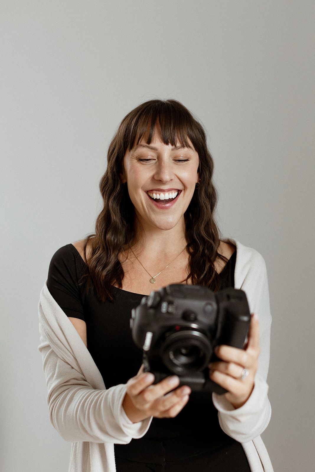 A photographer in black and white clothing smiles while examining their camera.