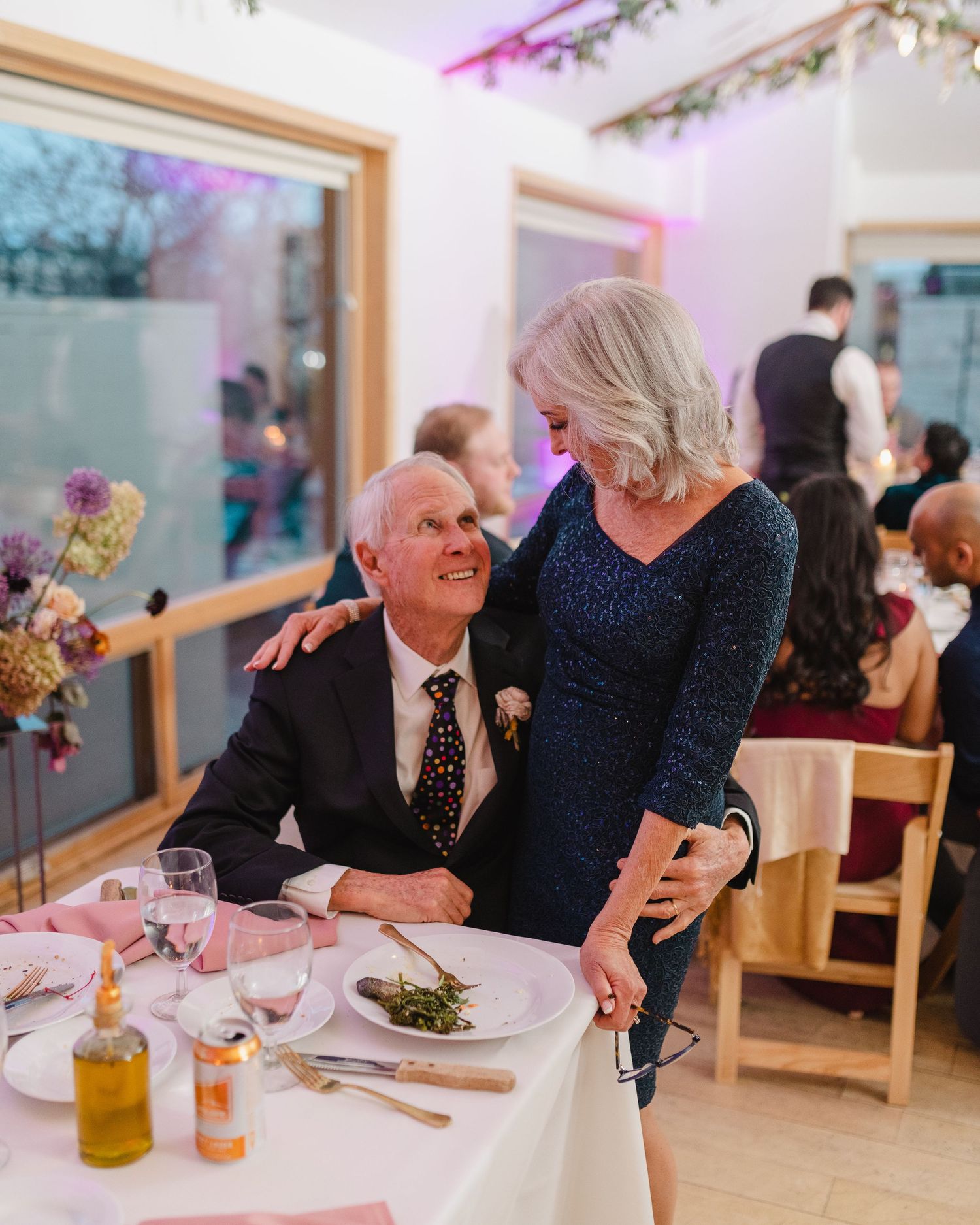 A couple shares an intimate moment at an elegant wedding reception with pink ambient lighting.