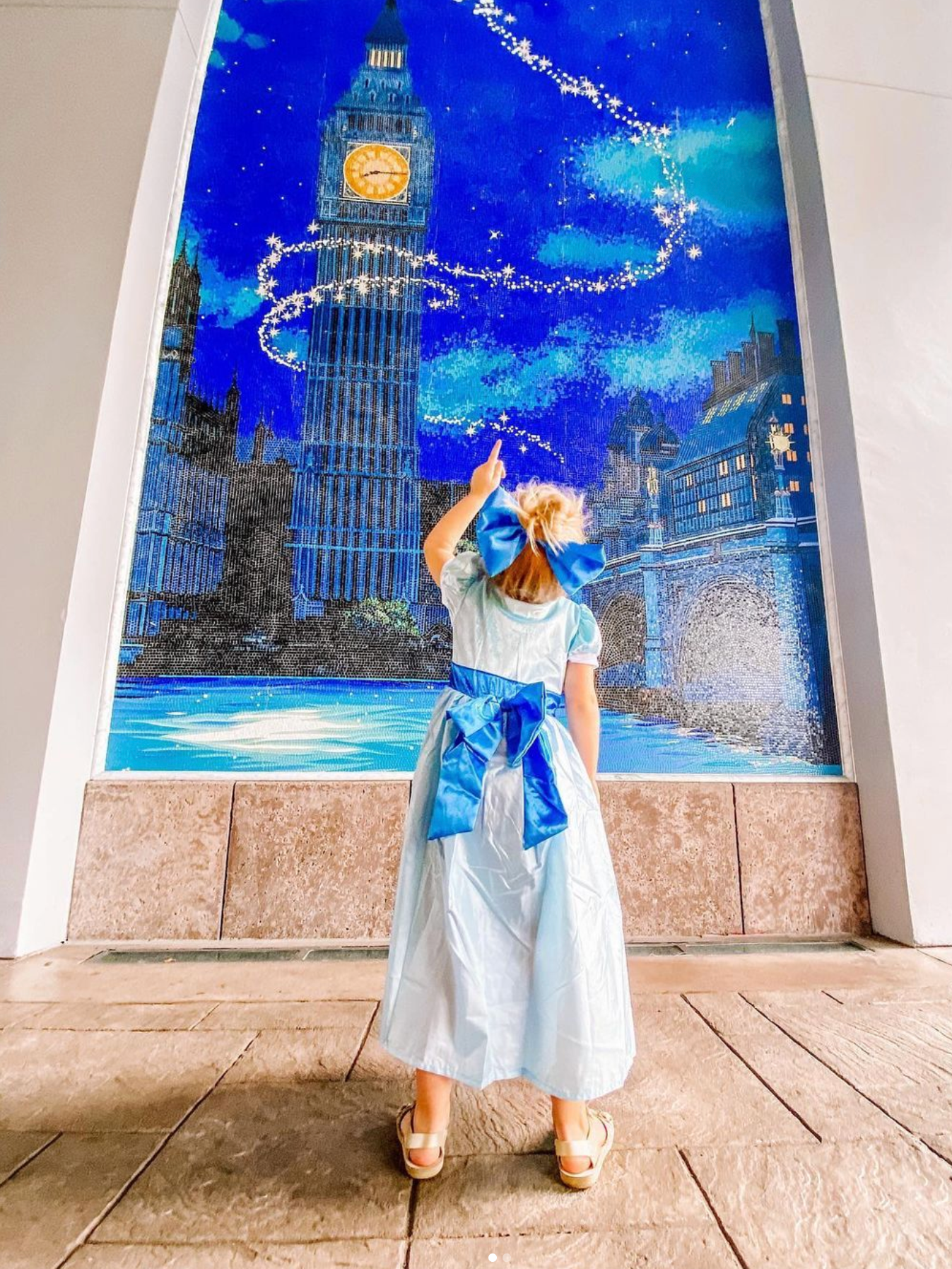 A figure in a white dress and blue sash poses in front of Big Ben with a magical glowing night sky backdrop.