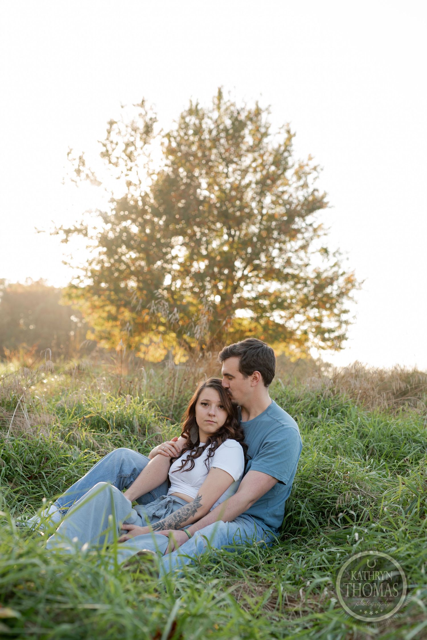A couple cuddles together on a grassy hillside during sunset.