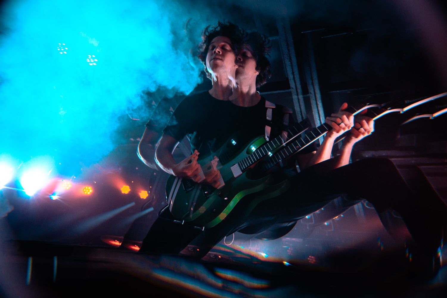 Concert performer silhouetted against blue stage lighting and smoke effects.