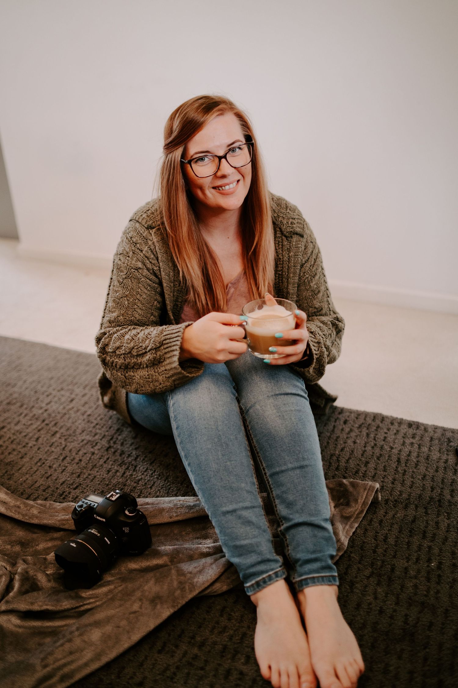 Person relaxing on dark couch wearing brown sweater and jeans holding coffee cup.