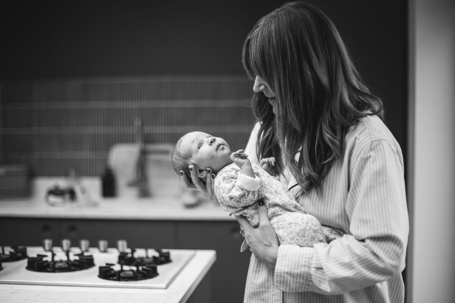 A tender moment between caregiver and newborn captured in black and white in a kitchen setting.