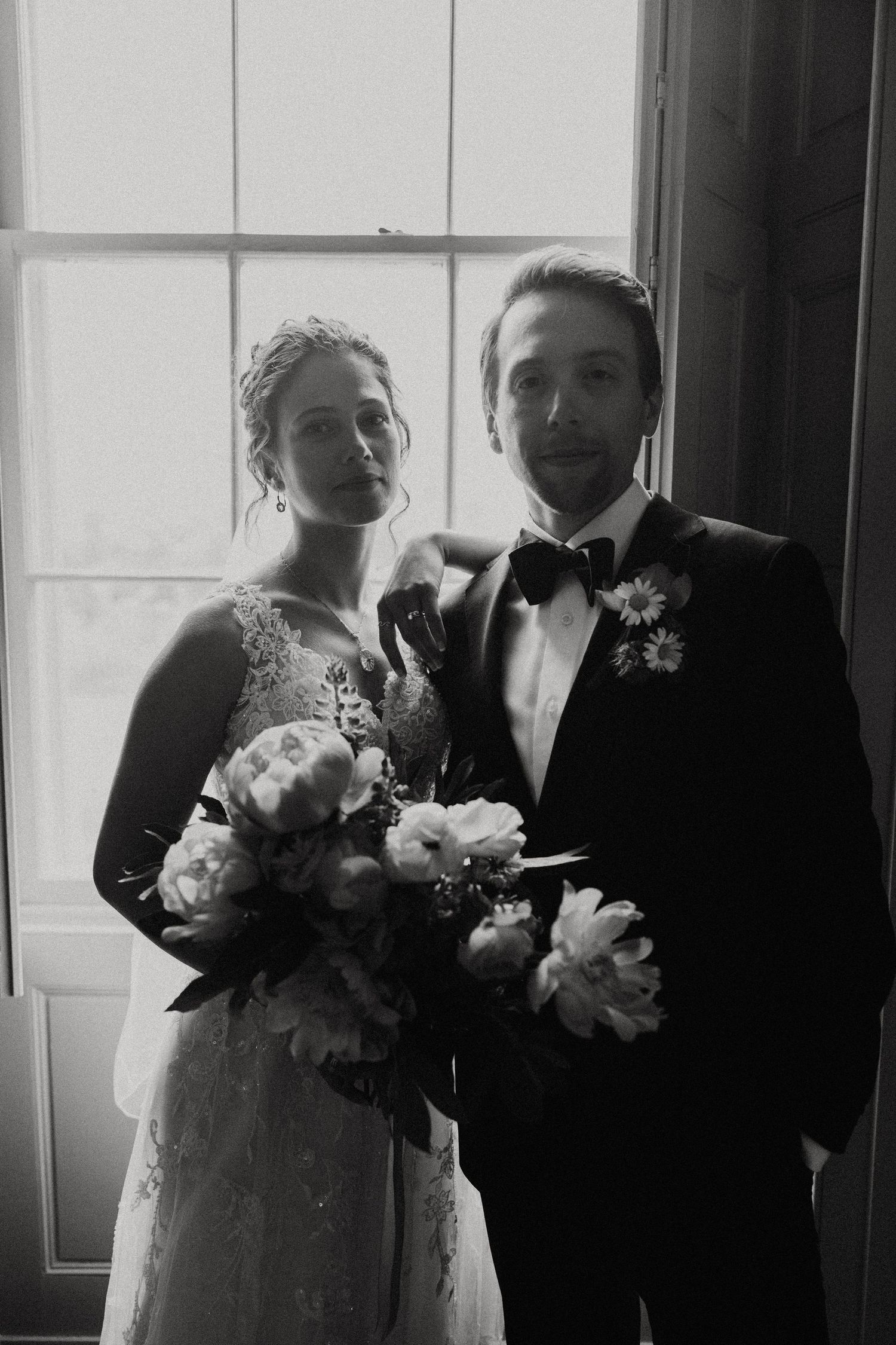 Bride and groom pose in black and white portrait by window with peonies bouquet. Westport Ma. Miranda Photo & Co