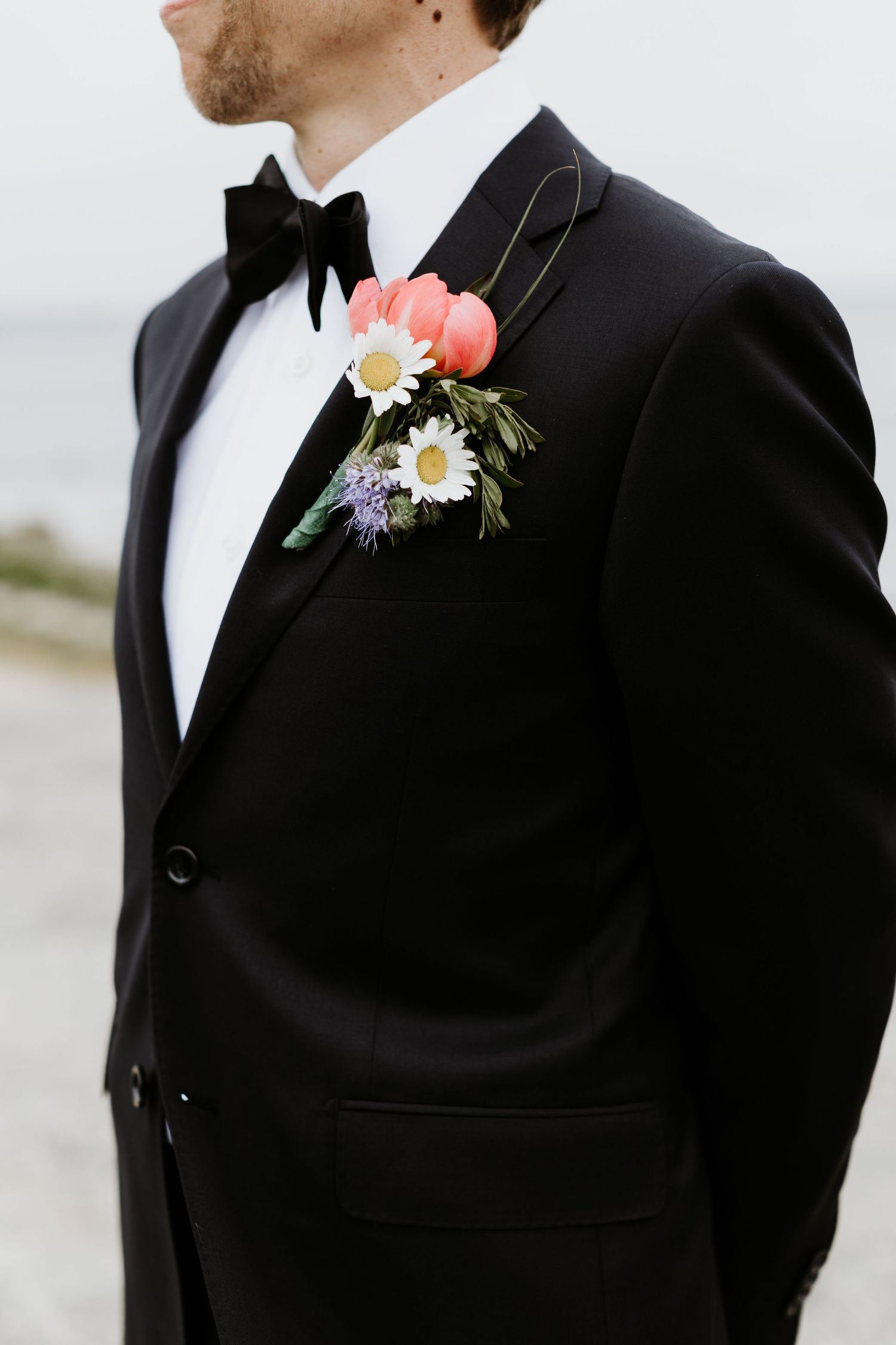 Close-up of groom in black tuxedo wearing a boutonniere with daisies, pink tulips, and lavender flowers. New Bedford, Ma. Miranda Photo & Co