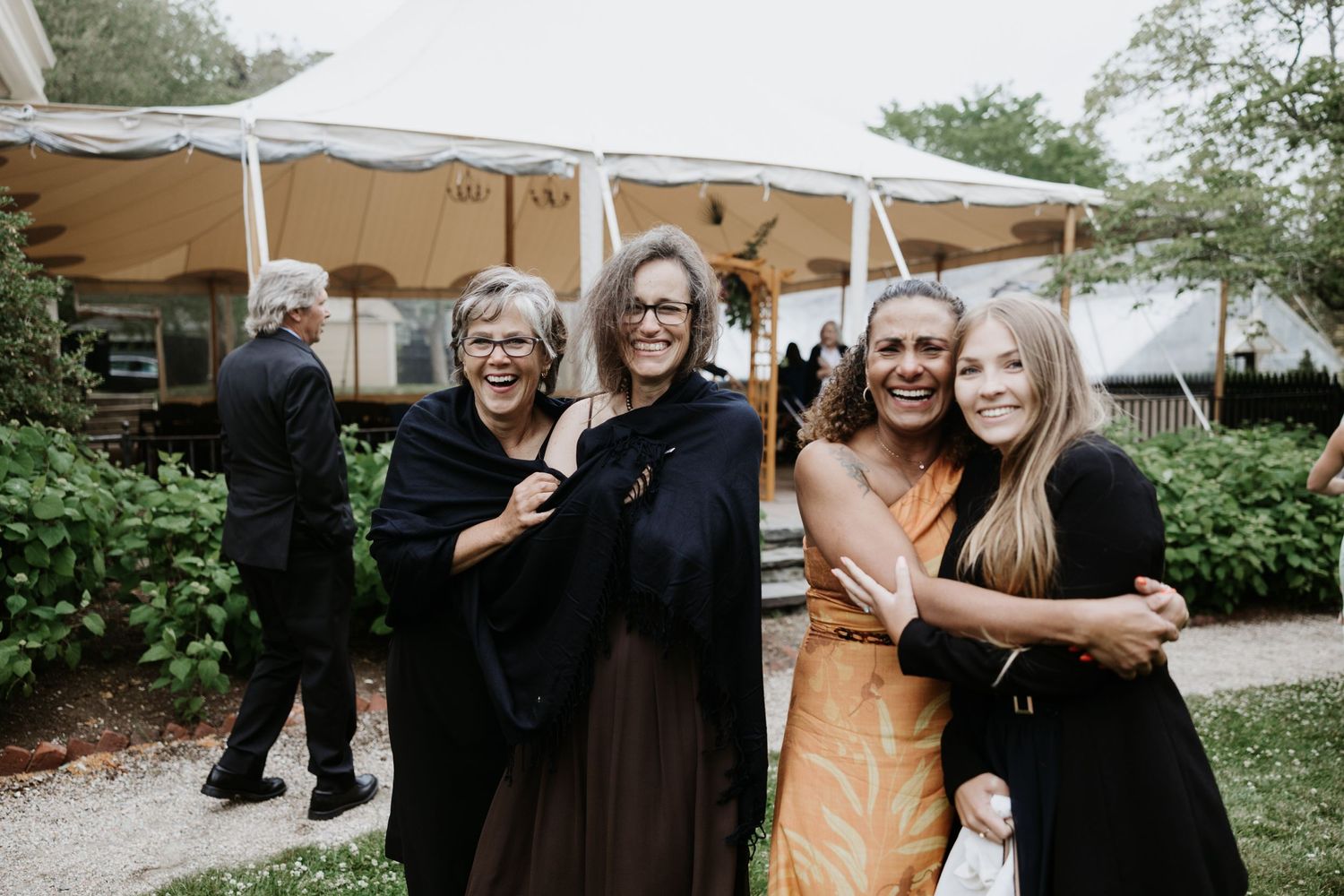 Four women smiling and embracing outdoors near a white wedding tent at a garden reception. New Bedford, Ma. Miranda Photo & Co