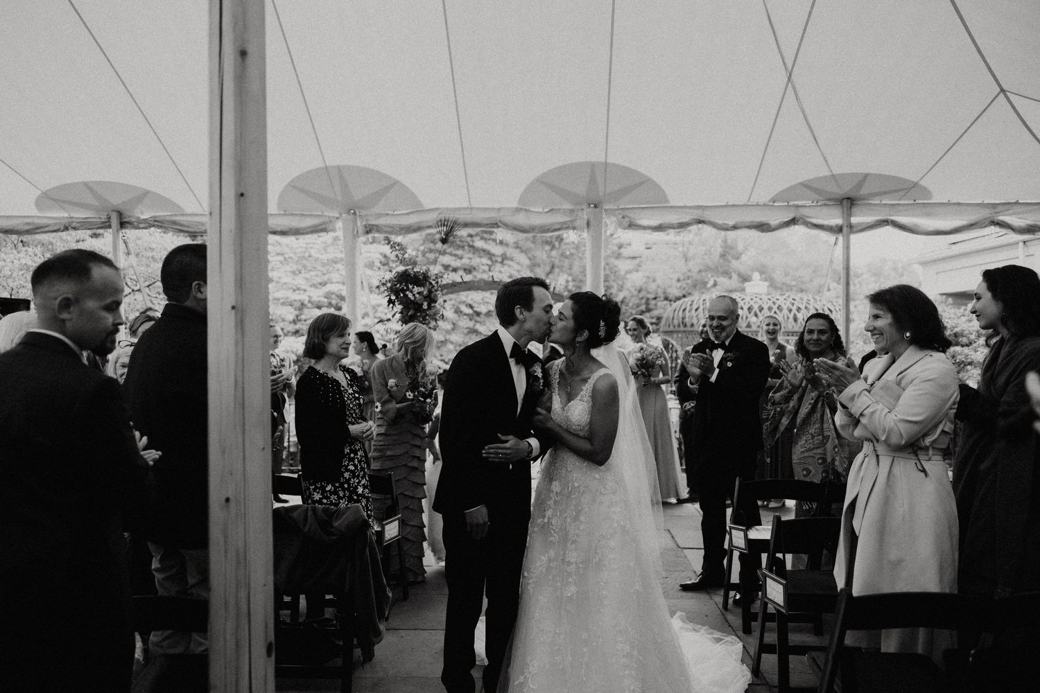 Bride and groom share first kiss at altar under white tent surrounded by wedding guests. Rotch Jones Duff House Miranda Photo & Co