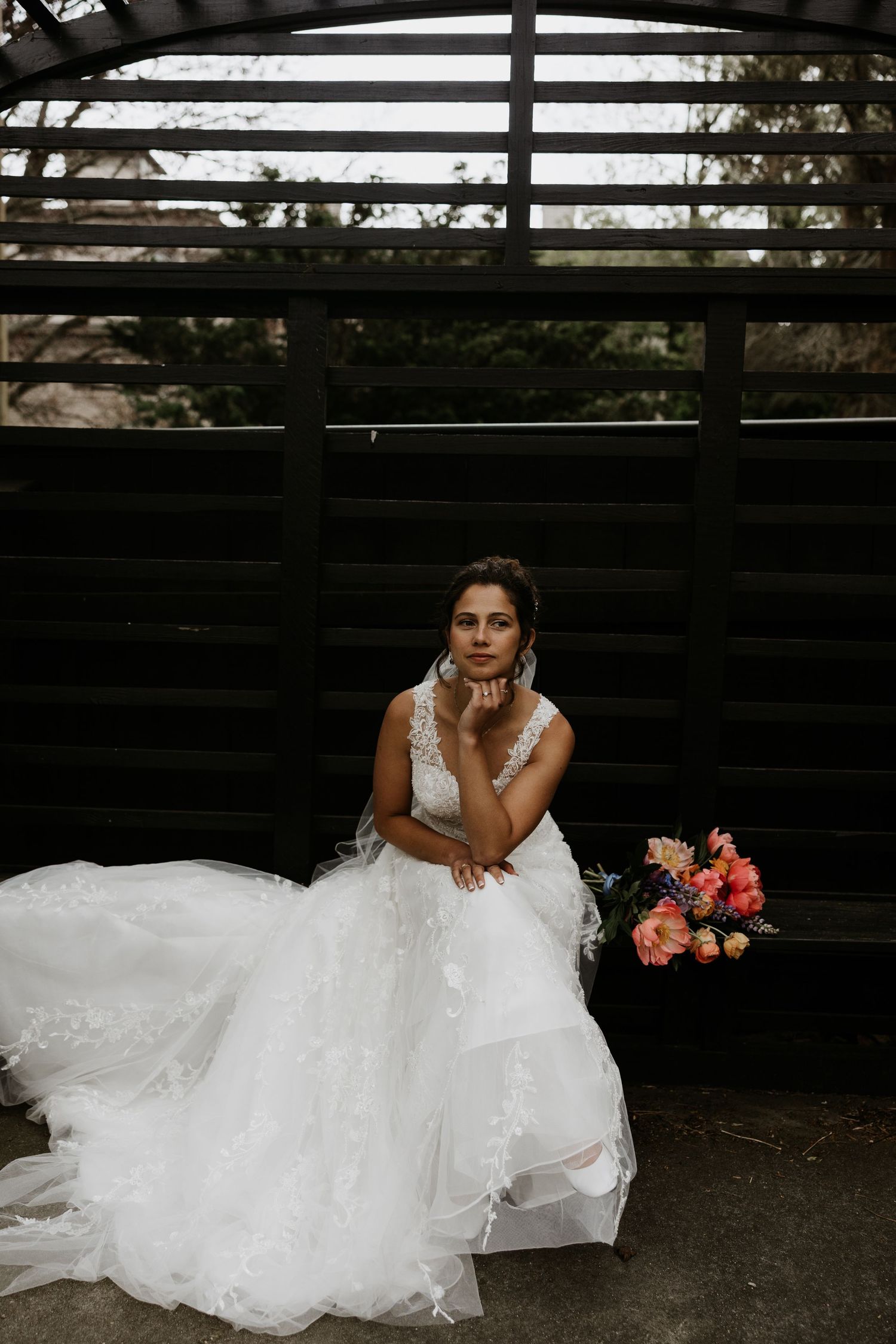 Bride in a lace wedding gown seated alone on a bench with a colorful bridal bouquet beside her. New Bedford, Ma. Miranda Photo & Co