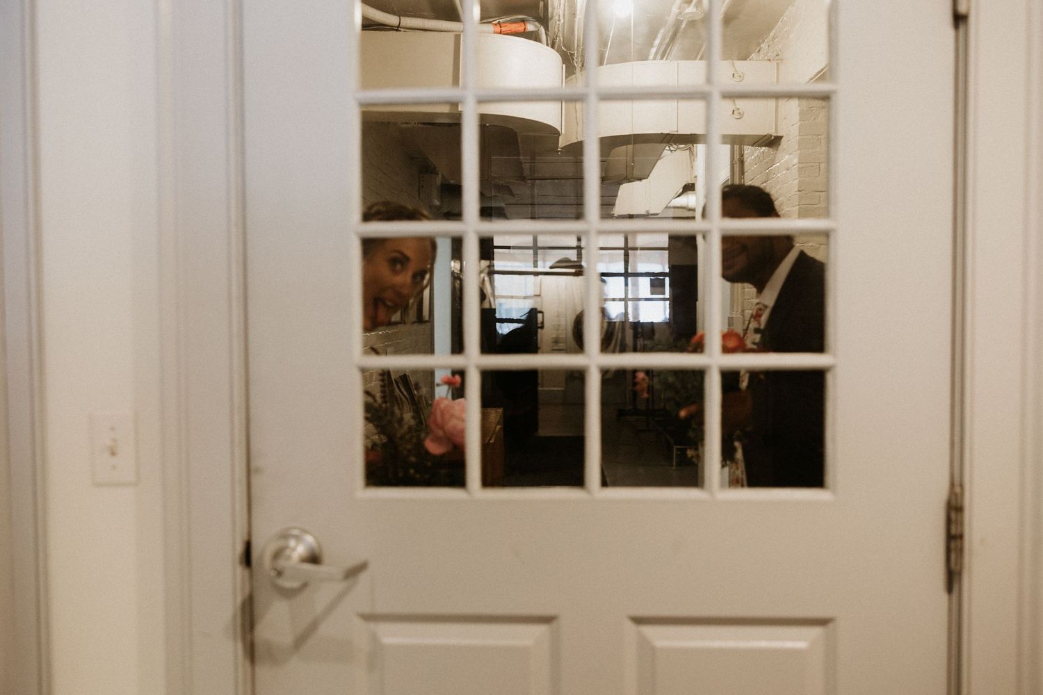 Wedding guests peeking through a white French door with glass panels at a wedding venue. New Bedford, Ma. Miranda Photo & Co