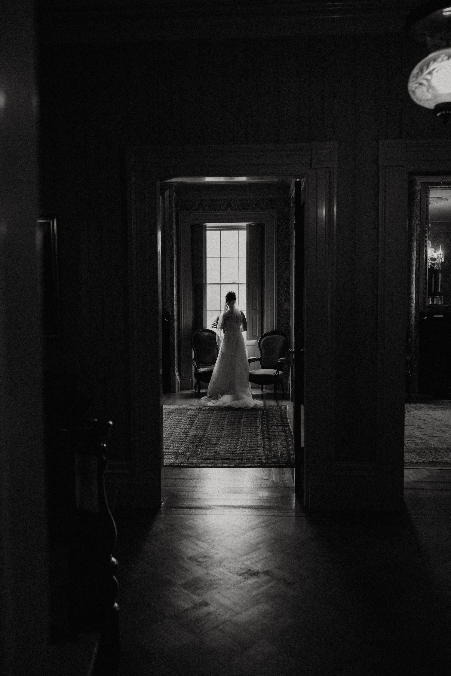 Dramatic black and white silhouette of bride in wedding gown standing in a doorway bathed in window light. New Bedford, Ma. Miranda Photo &