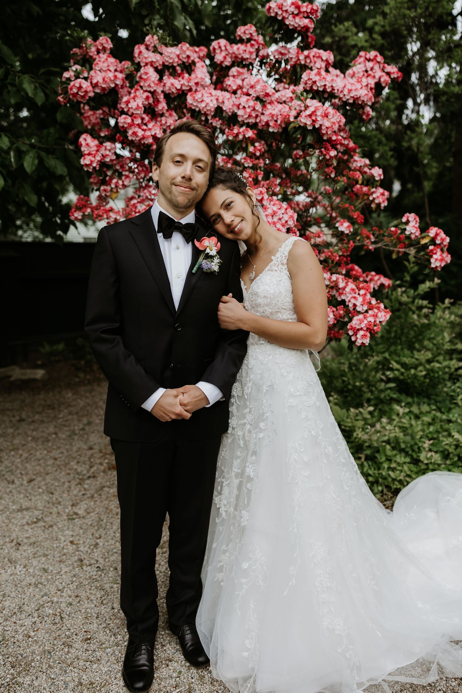 Bride and groom posing together in front of vibrant pink flowering trees in a lush garden. New Bedford, Ma. Miranda Photo & Co