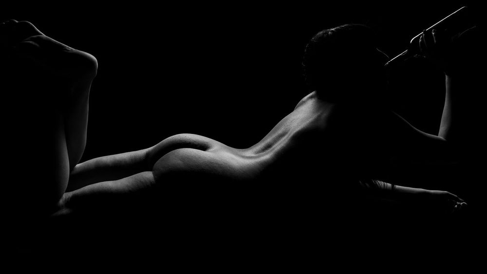 Artistic black and white nude study highlighting curved silhouette against dark background.